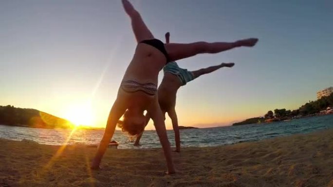 两个青少年在日落海滩慢动作做侧翻