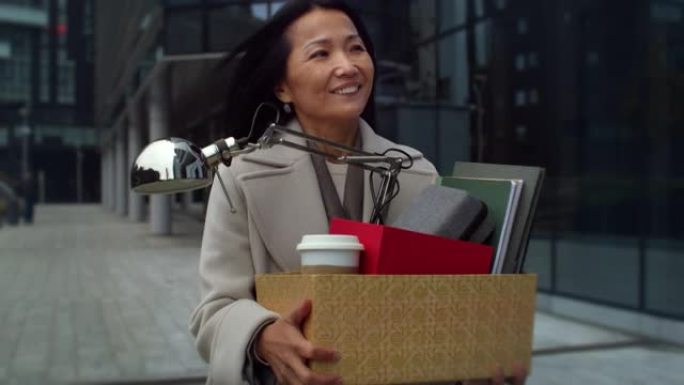 优雅的亚洲中年女商人的肖像走在早晨，拿着一盒她的办公用品。女性员工搬迁，换工作，对新的职业机会感到高