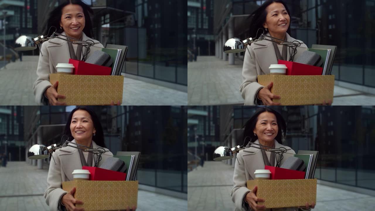 优雅的亚洲中年女商人的肖像走在早晨，拿着一盒她的办公用品。女性员工搬迁，换工作，对新的职业机会感到高