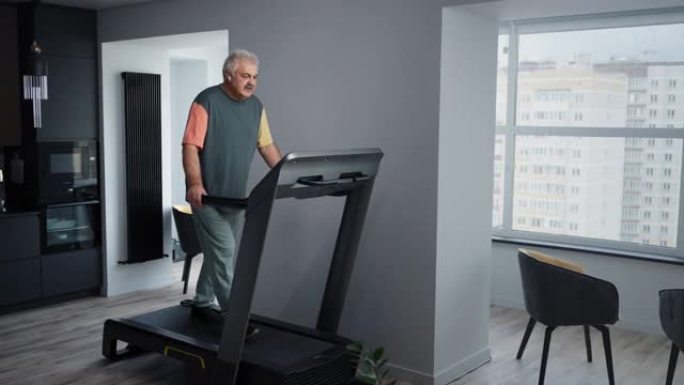 活跃的高级男子在家跑步机上锻炼时用耳机听音乐