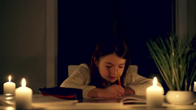 女学生在烛光下的抄写本上写字，在黑暗的房间里学习课程