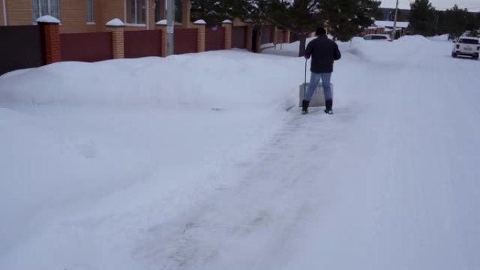 冬天，一个人在房子的院子里打扫雪。一名男子用铲子扫雪