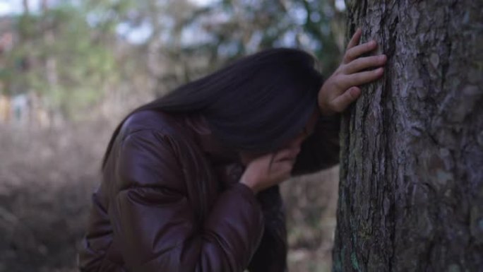 痛苦的女人靠在树上，用手遮住嘴感到恶心。人因为创伤后悔而想呕吐