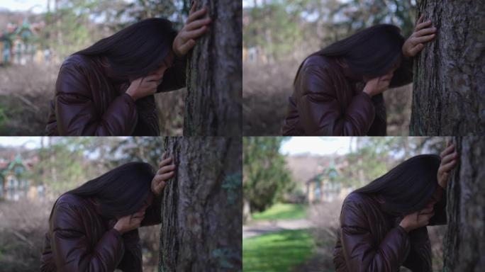 痛苦的女人靠在树上，用手遮住嘴感到恶心。人因为创伤后悔而想呕吐