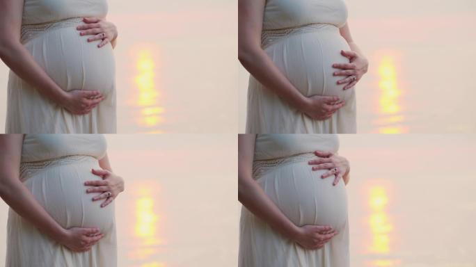 一名孕妇站在床后的海边，特写镜头，抚摸着她的肚子