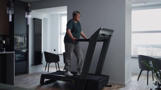 积极的老年妇女在家训练，在客厅的跑步机上行走，老年人的有氧运动