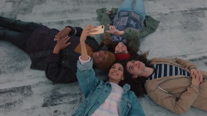 快乐的朋友躺在屋顶上闲逛，使用智能手机相机拍摄自拍照片，一起享受共享周末