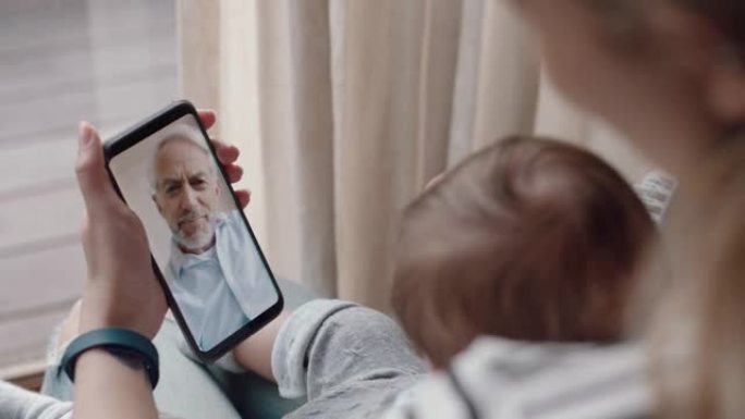 年轻的母亲和婴儿与祖父进行视频聊天，使用智能手机挥舞着新生婴儿，享受家庭联系
