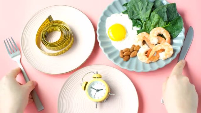 三盘食物，闹钟和厘米胶带和粉红色背景上的女性手间歇性禁食概念。