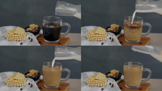 在灰色背景下桌子上的华夫饼旁边的咖啡杯中倒入牛奶的特写镜头