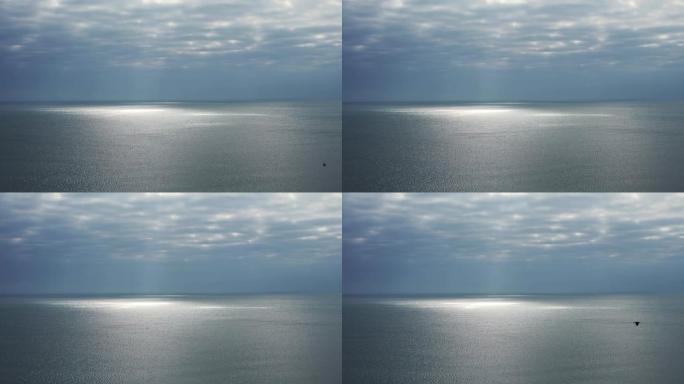 迷人的海景。多云的天空几乎与地平线上的大海融合在一起，太阳的光线穿过并在海面上留下发光的斑点