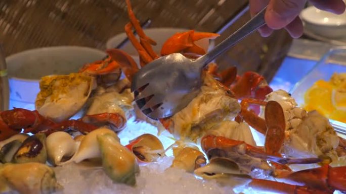 男人的手在豪华的海鲜自助餐中使用金属钳从冰上取出煮熟的螃蟹