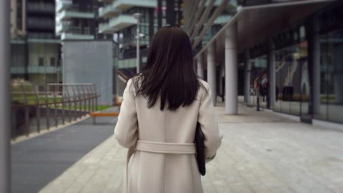 优雅的女商人在早晨走向办公室的背影。女项目经理走在街上，准备开始一天的工作，为公司会议考虑创新的想法