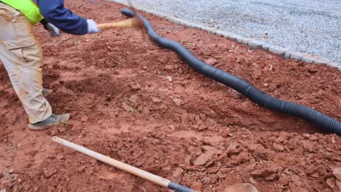 一名工人挖了一条沟渠，以便在大雨期间铺设雨水排水管，以排干该地区