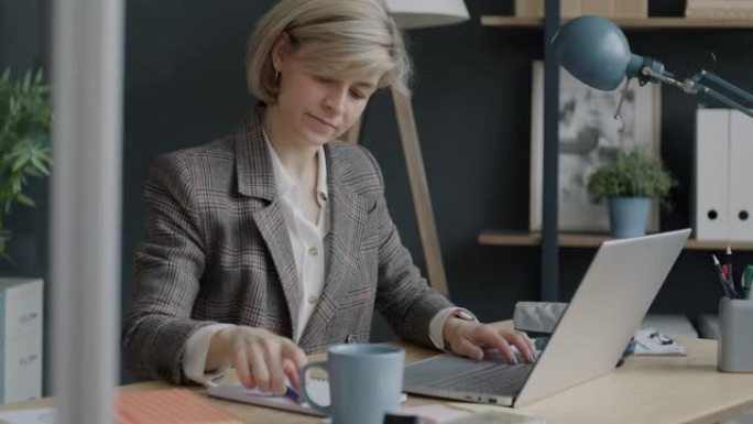 有动力的女商人在办公室里用笔记本电脑工作并在笔记本上写字的肖像