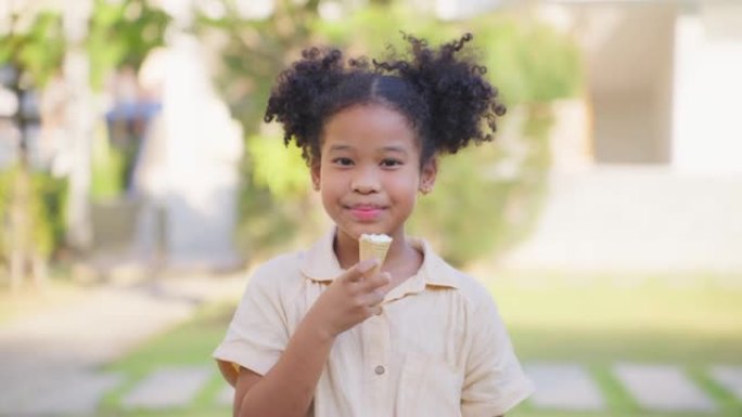 非裔美国小女孩在花园里吃冰淇淋的肖像。年轻可爱的孩子站在户外，拿着甜蜜的甜点，微笑着，看着相机，感到