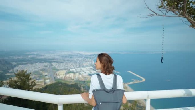 游客站在观景台上，寻找蓝色背景山谷景观模型。时髦的年轻女孩穿着便服，欣赏从山到海和安塔利亚市的景色。