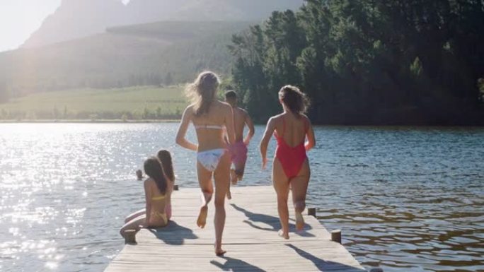 一群朋友在日落时从湖边码头跳下来，玩得开心，在水中嬉戏，享受自由分享夏季冒险
