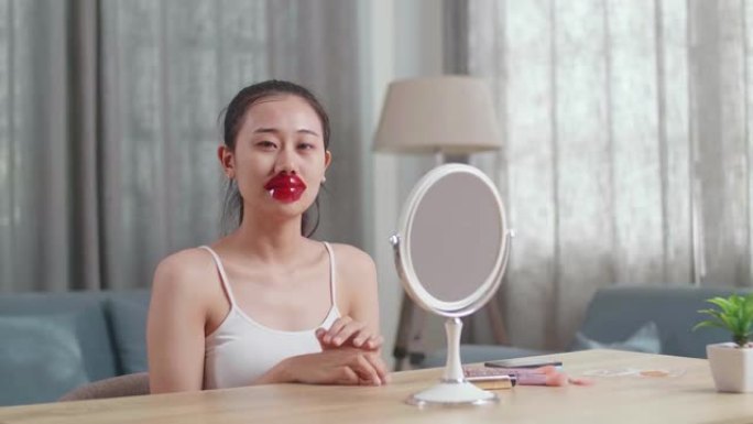 美丽的年轻亚洲女子照镜子使用胶原蛋白唇膜干燥干裂的嘴唇和微笑对着镜头在家照顾她的皮肤