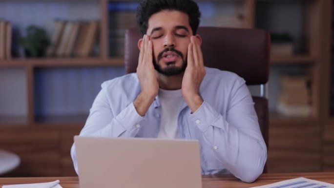强调阿拉伯男子在笔记本电脑触摸头部，在现代办公室的工作场所遇到问题。危机和创业业务问题，令人头疼的概