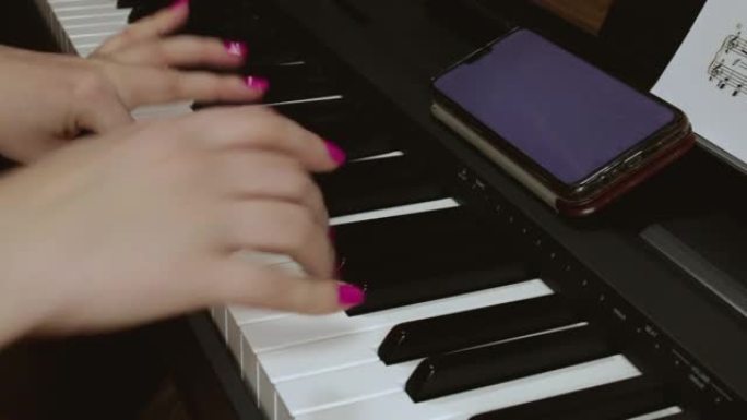 一名妇女根据手机和纸上记录的音符弹奏电子钢琴。钢琴和女性手的特写镜头