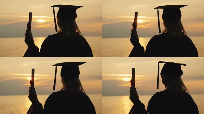 一个男人手里拿着文凭，一个毕业生的衣服看着海上的日出