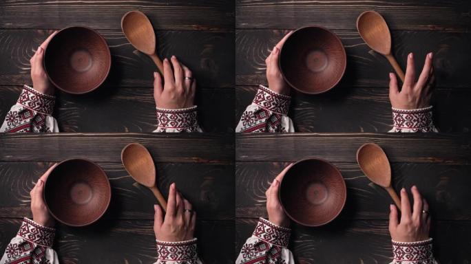 带勺子的空粘土碗。乌克兰妇女坐在国家餐厅等待点菜。女孩在等待盘子时紧张地敲手指在木桌上。