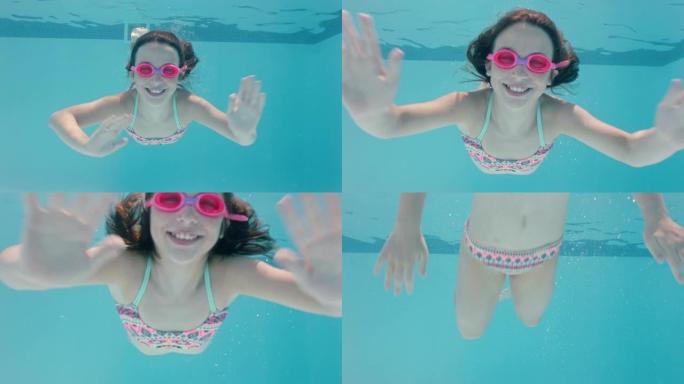 快乐的女孩在游泳池水下游泳微笑挥手享受在水晶般清澈的水中游泳戴着护目镜享受夏天4k