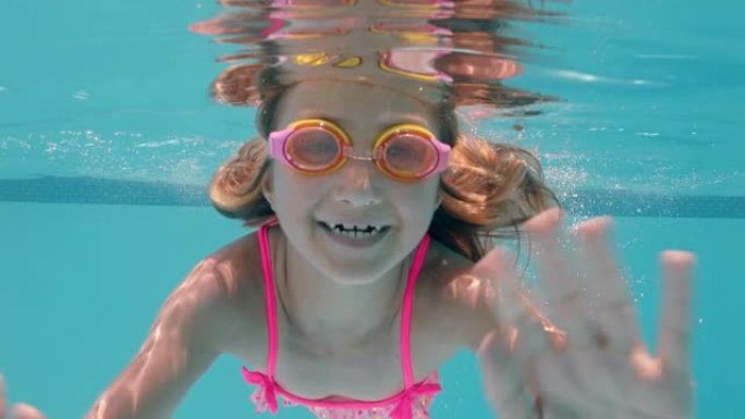 快乐的小女孩在游泳池水下游泳微笑挥手享受在水晶般清澈的水中游泳戴着护目镜享受夏天4k