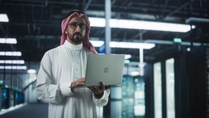 穆斯林数据中心IT工程师站在一个带有操作服务器机架的房间里。云计算架构师使用笔记本电脑为网络安全和数