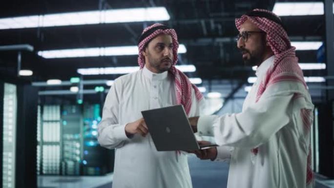 在现代数据中心: 中东AI工程师和IT专家在服务器机房工作，与笔记本电脑交谈，进行系统维护检查。专家