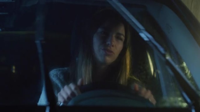 一个年轻女子在雨夜开车的肖像。女司机唱歌，谨慎，遵守规则，在娱乐的同时检查后视镜