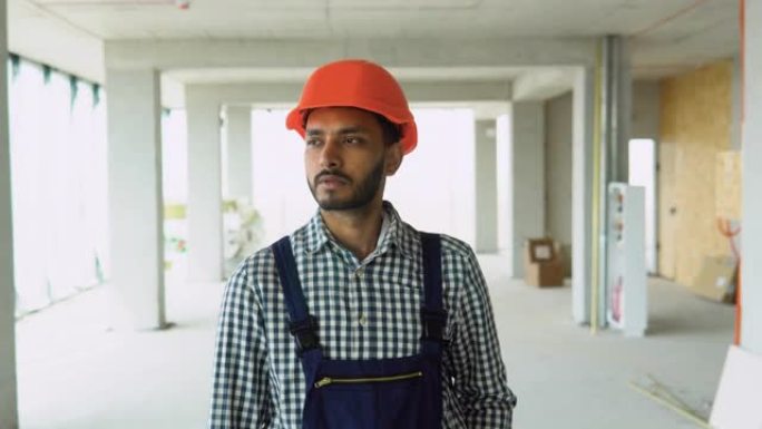 穿着制服和头盔的印度亚裔建筑工程师在办公中心的建筑工地行走