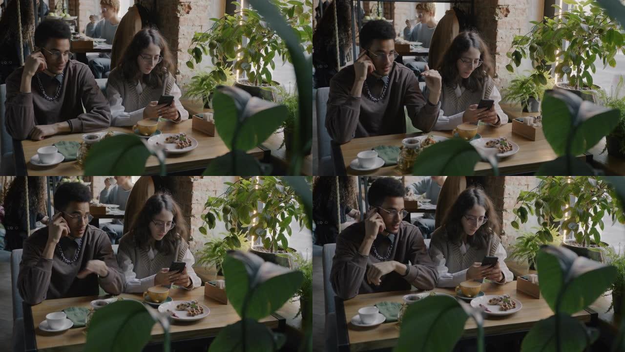 非洲裔美国男子在手机上讲话，而白人女友在咖啡馆使用智能手机发短信