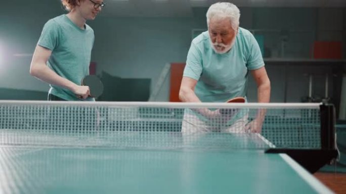 经验丰富的老人教孙子在俱乐部打乒乓球时如何正确握住球拍。祖父教十几岁的男孩打乒乓球