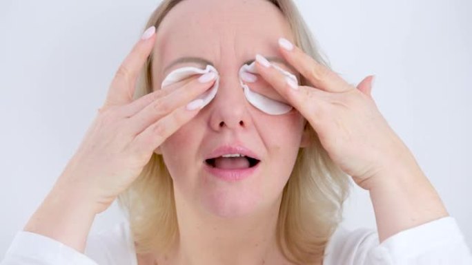 一名妇女将海绵放在眼睛上并摩擦手指卸妆洗掉化妆品晚上的日常程序在白色背景上化妆后的白色修指甲中年妇女