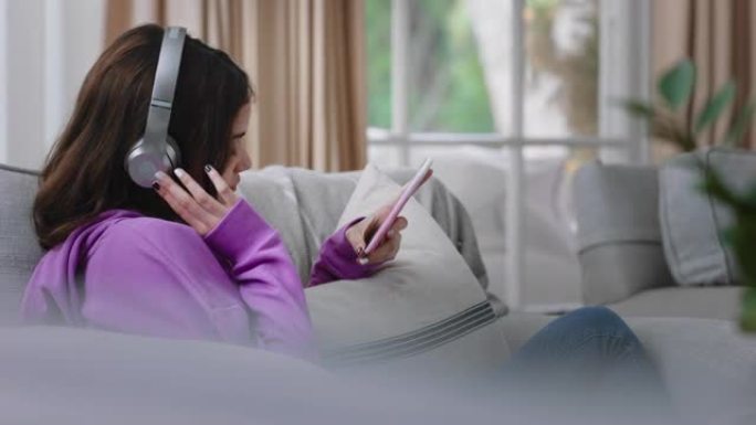 快乐的少女戴着耳机听音乐，在家沙发上放松，用智能手机发短信，享受在社交媒体上分享生活方式