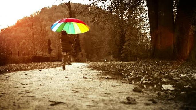 明亮的暖色调镜头: 快乐的小男孩在秋天的公园里用雨伞跳