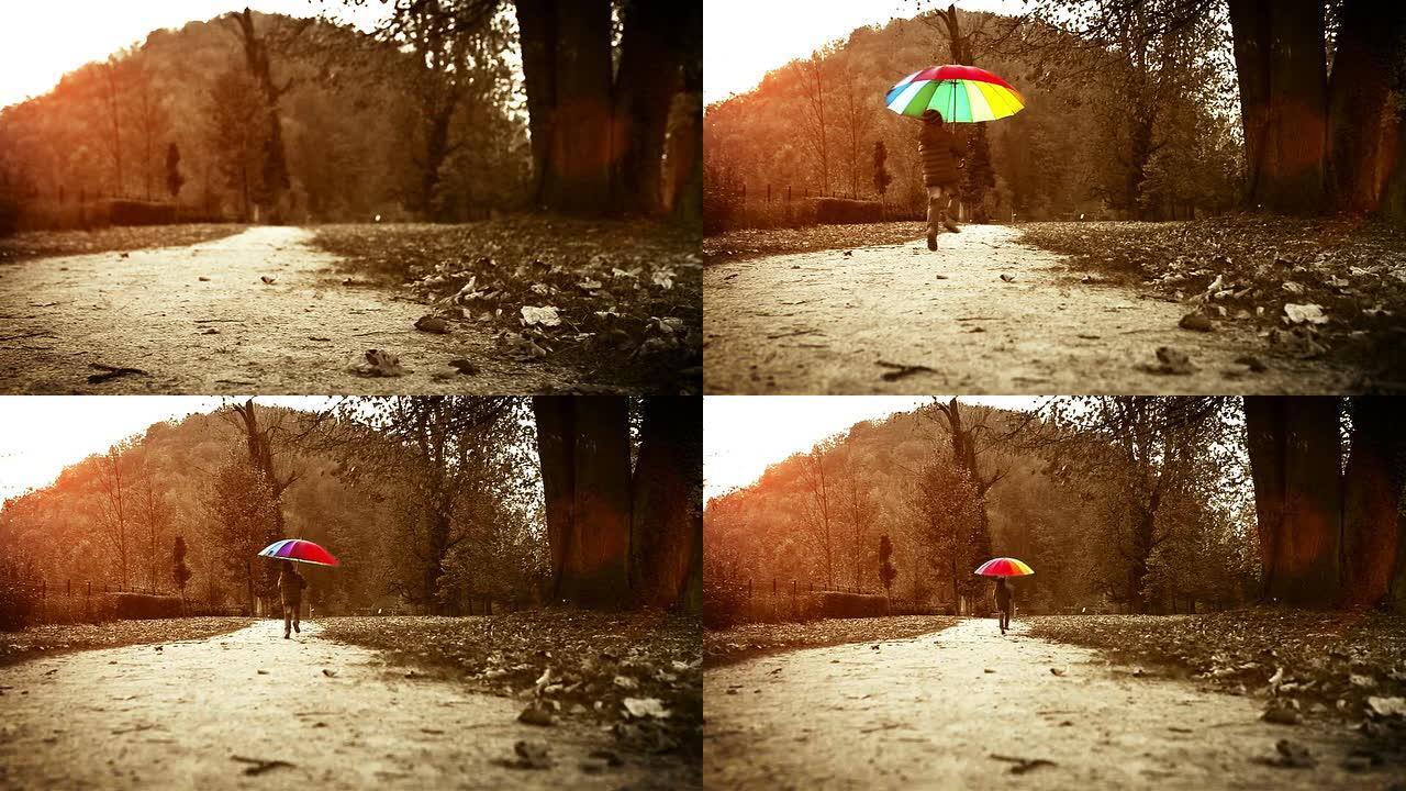 明亮的暖色调镜头: 快乐的小男孩在秋天的公园里用雨伞跳