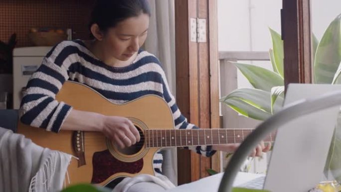 年轻的亚洲女性在家弹吉他有抱负的音乐家学习用笔记本电脑演奏乐器享受创造性的表达练习音乐