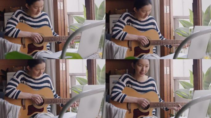 年轻的亚洲女性在家弹吉他有抱负的音乐家学习用笔记本电脑演奏乐器享受创造性的表达练习音乐