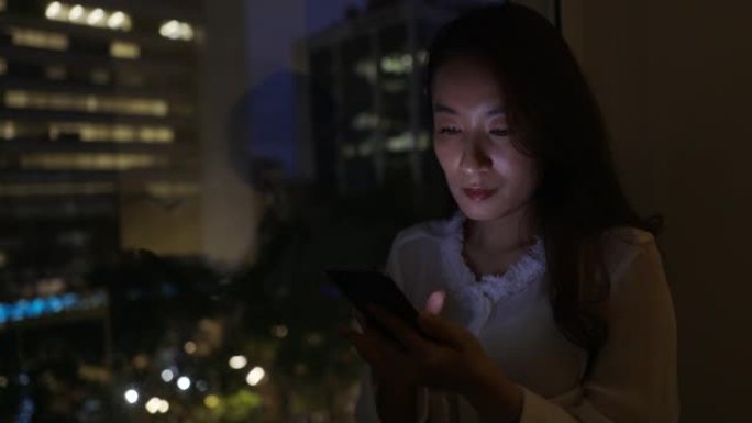 亚洲女商人在办公室加班，并使用手机与远程客户和同事进行通信。