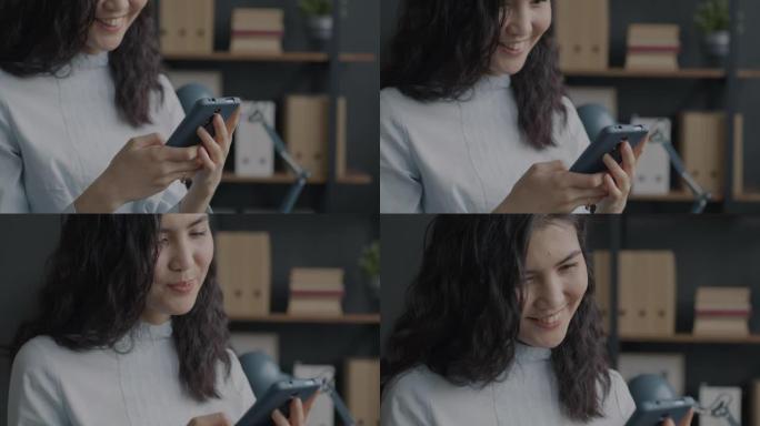 穿着考究的亚洲女商人用智能手机发短信并在办公室微笑的慢动作