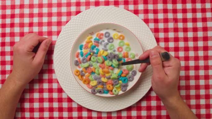 一个孤独的人的手的俯视图在早餐时吃五颜六色的谷物，食欲不振。