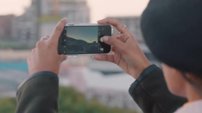 年轻女子使用智能手机移动相机拍摄城市照片，享受观光在社交媒体上分享度假照片