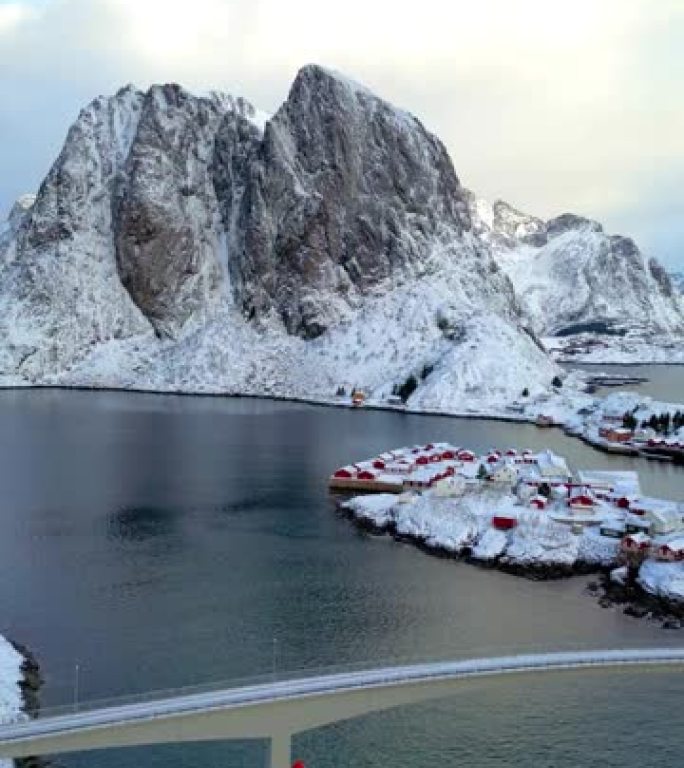 挪威罗弗顿岛鸟瞰图。瑞恩日出渔村的冬季与雪景山峰反映在水面上。挪威拥有红色的rorbu房屋。冬天下雪