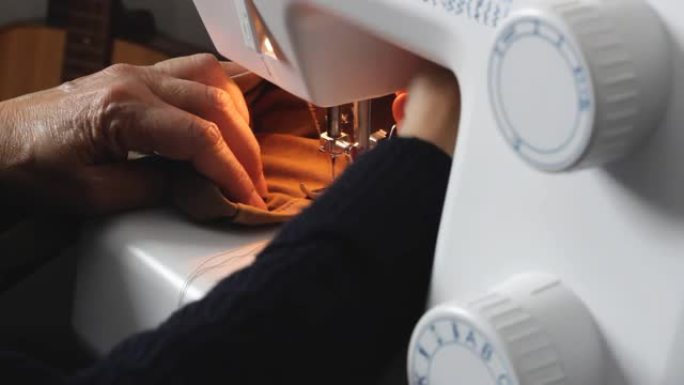 用家用缝纫机将一名老年妇女的手缝在材料上的特写镜头，然后用剪刀剪