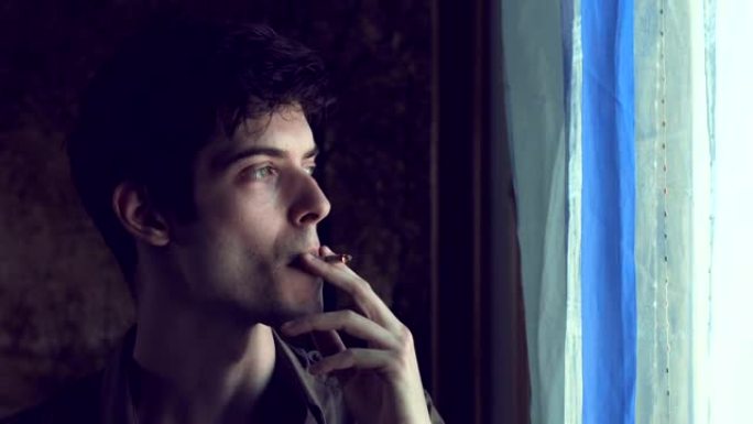 悲伤的年轻人在窗户附近吸烟