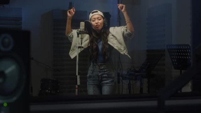 一位专业亚洲女歌手在录音室录制歌曲的肖像。美丽的年轻艺术家喜欢表演她的新浪漫单曲，用富有表现力的面孔