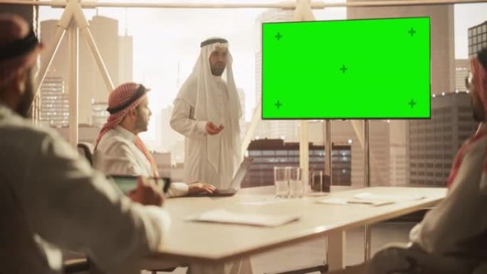 阿拉伯商人向一群沙特投资者展示数据。带有绿屏模拟显示的电视屏幕。现代办公室会议室商务会议演示